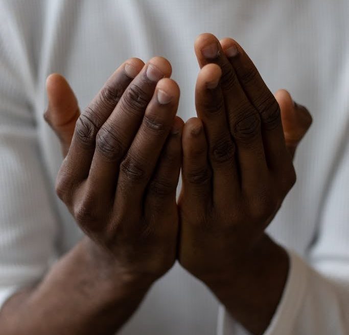 Selective focus of crop anonymous African American man wearing white turtleneck praying with open hands
