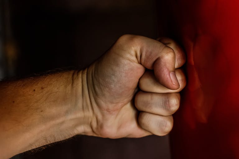 A detailed close-up of a clenched fist striking a red surface showcasing strength.