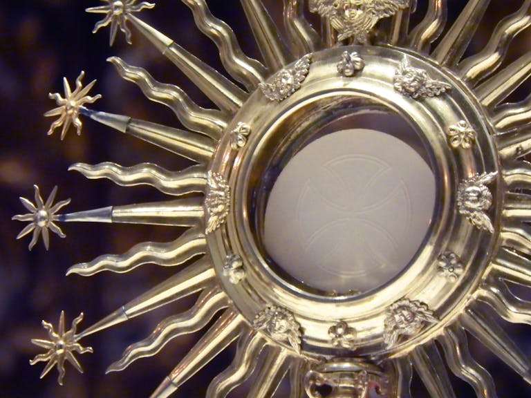 Close-up of a golden monstrance with a Eucharistic host in a church setting.