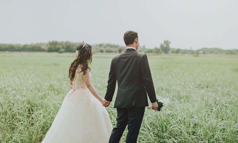 Couple holding hands in a serene field, perfect wedding photoshoot moment.