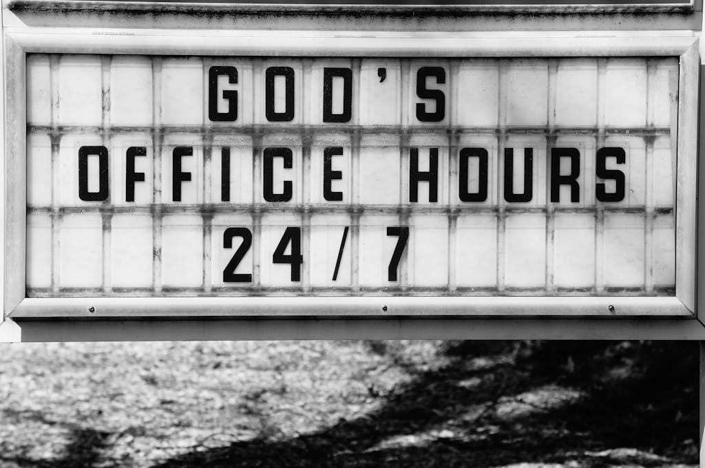 Monochrome photo of a church sign reading 'God's Office Hours 24/7' in Raleigh, NC.