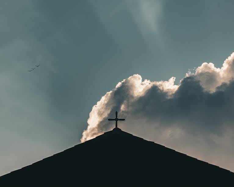 A cross silhouetted against dramatic clouds, evoking themes of spirituality and faith.