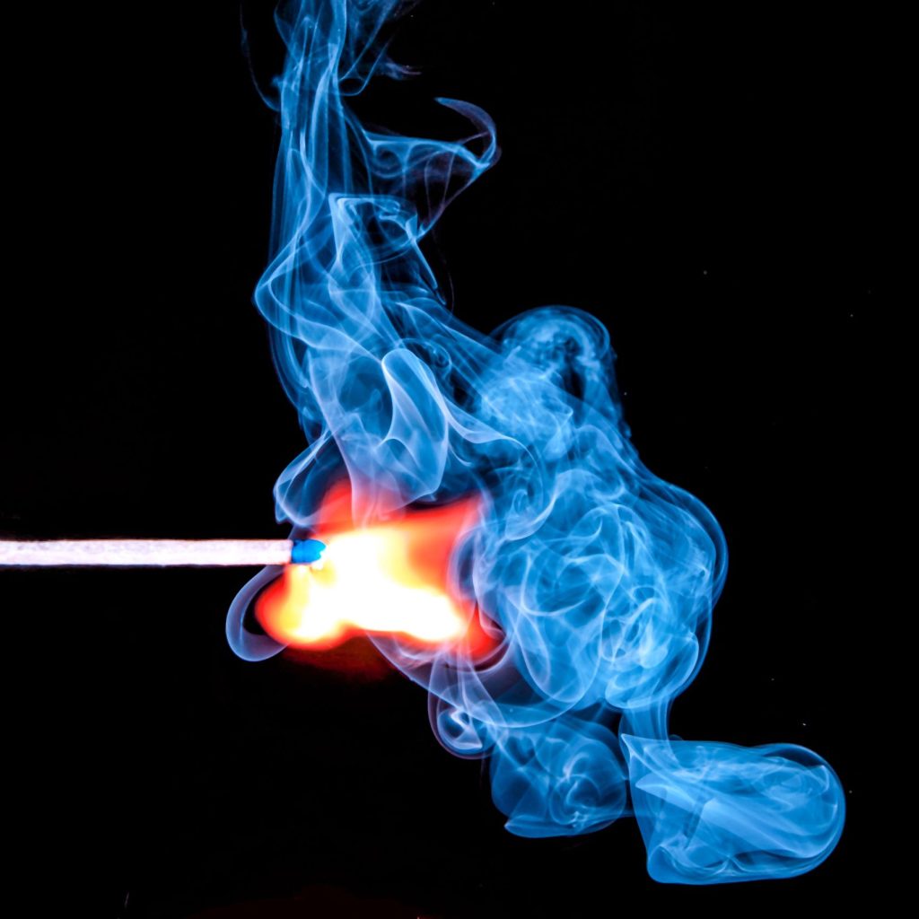 A match ignites with vibrant blue smoke against a black background.