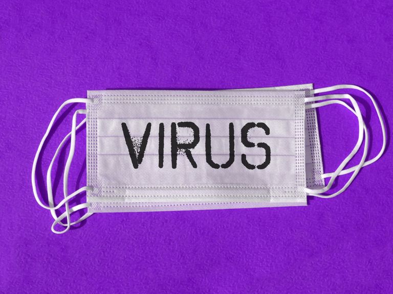 Close-up of a surgical mask with 'Virus' text against a purple backdrop symbolizing pandemic protection.