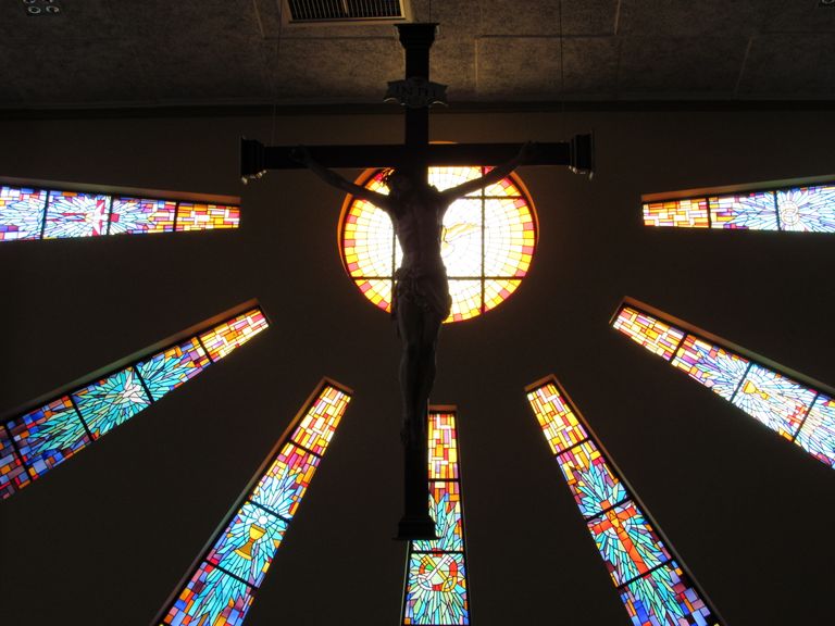 Silhouette of Jesus on the cross framed by vivid stained glass, evoking spiritual reflection.